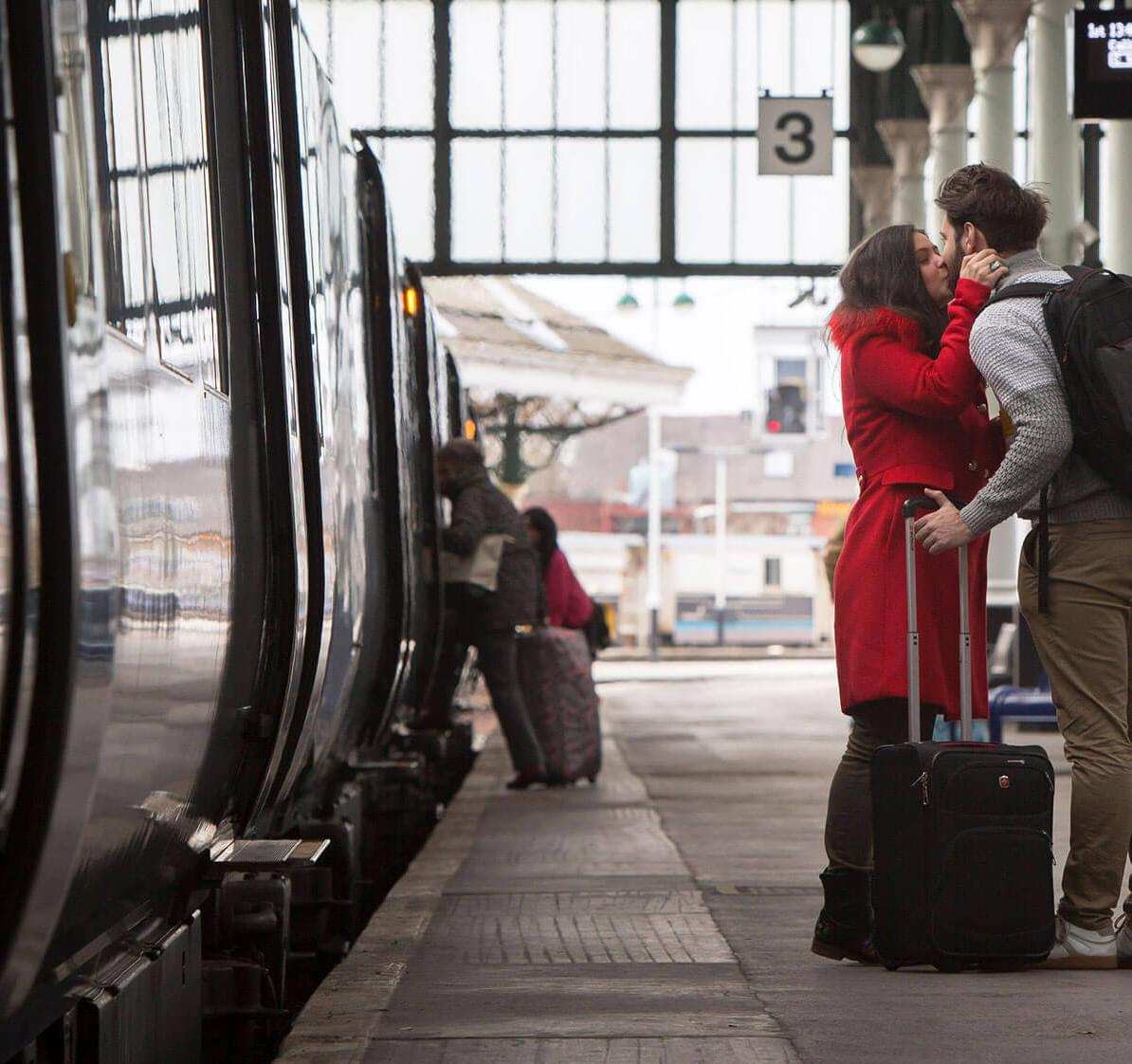 A couple kiss goodbye next to a train
